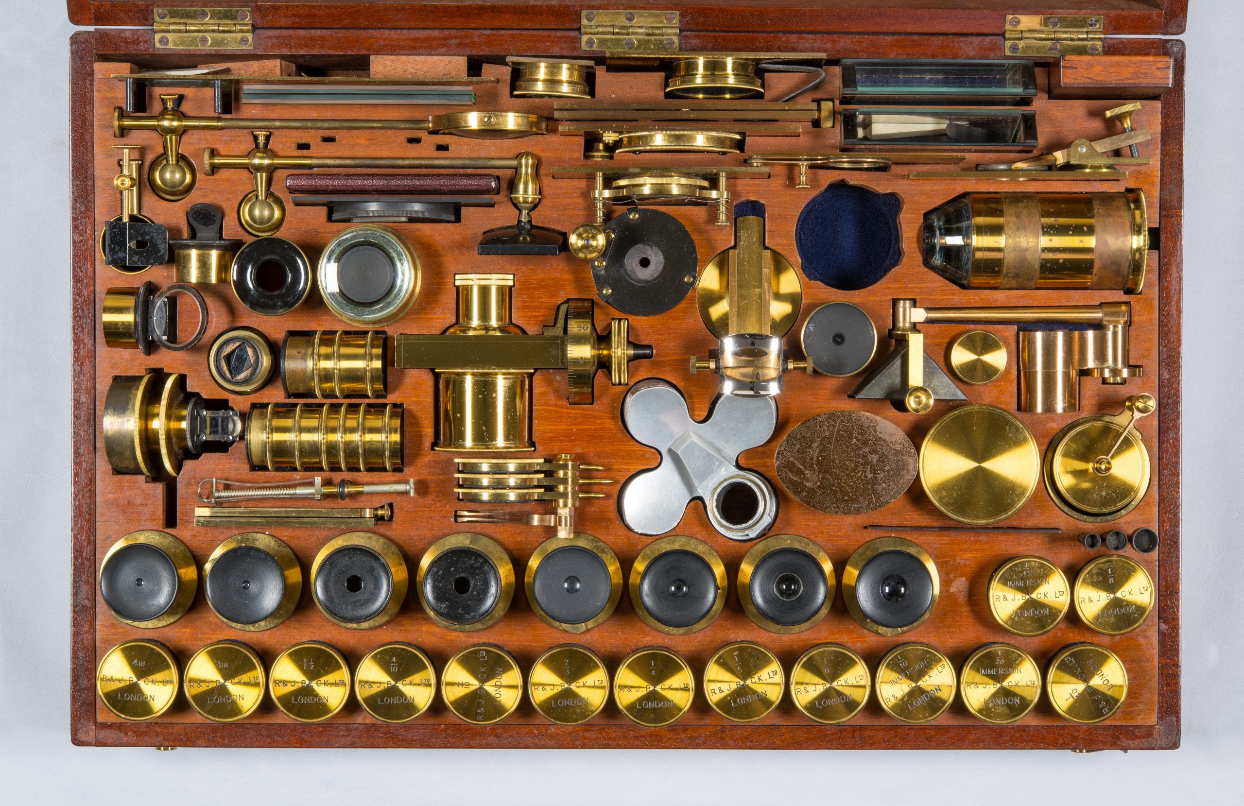 A wooden box full of different attachments and lens for the beck microscope.